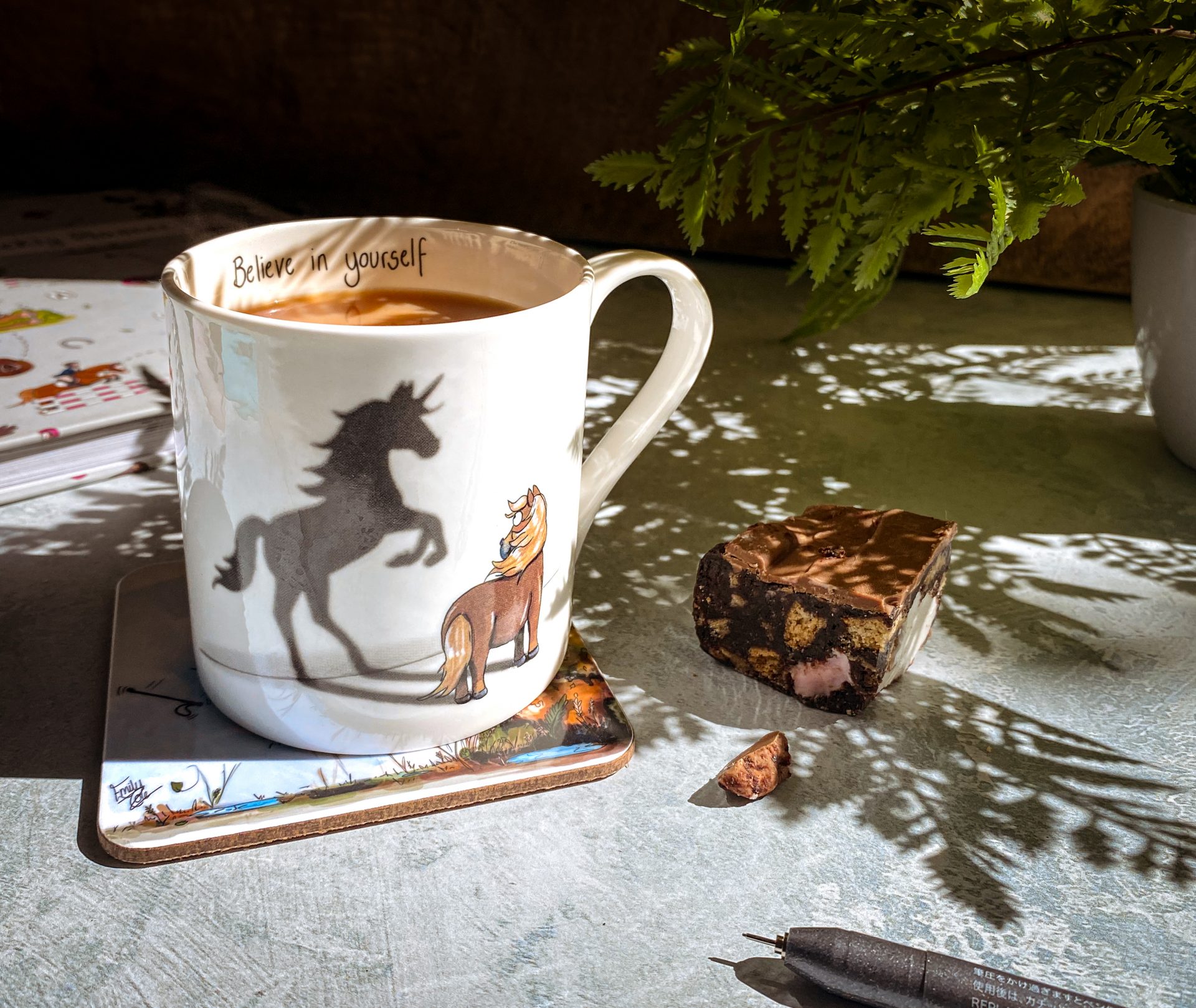 Image of Emily Cole's 'Believe in Yourself' Fine Bone China Mug, featuring a flaxen pony gazing at its unicorn shadow. An inspiring quote ' Believe in yourself' written along the inside rim.