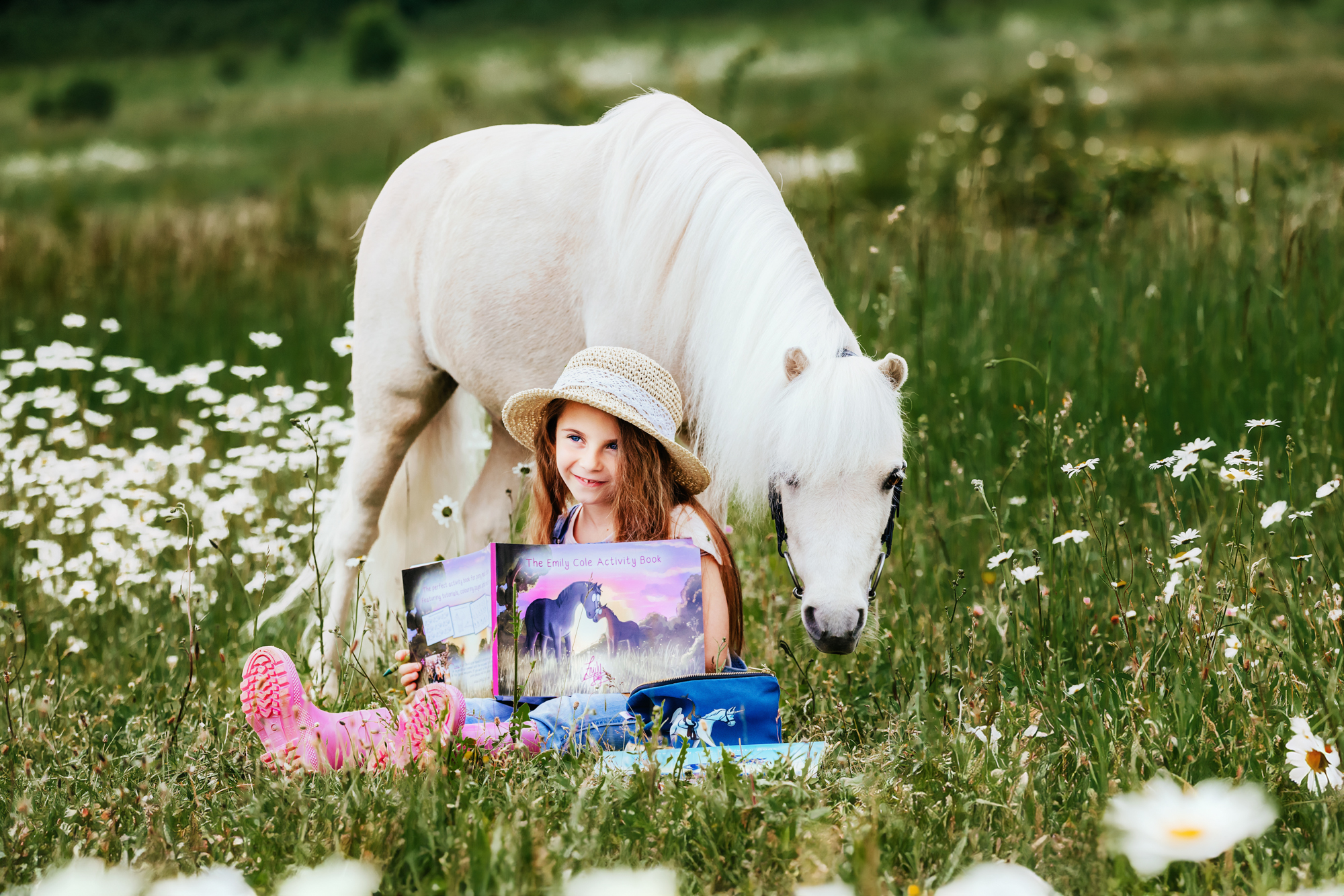 little girl smiling holding the emily cole activity book for children open. A small pony is stood behind her